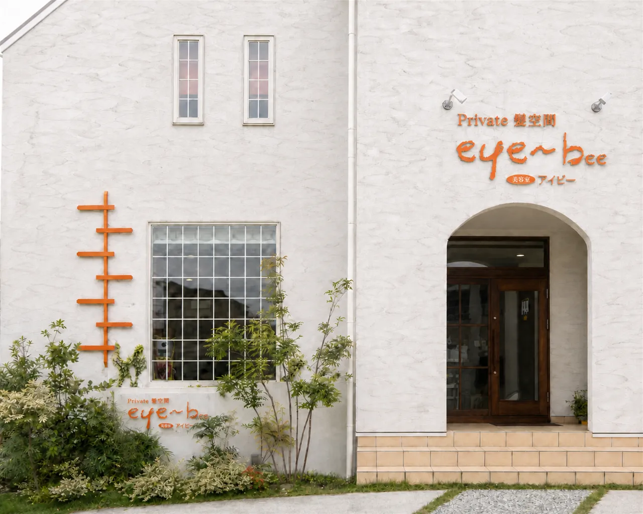 美容室アイビーの白い外観。切妻屋根とアーチ型の木製ドアを正面から見た様子。
