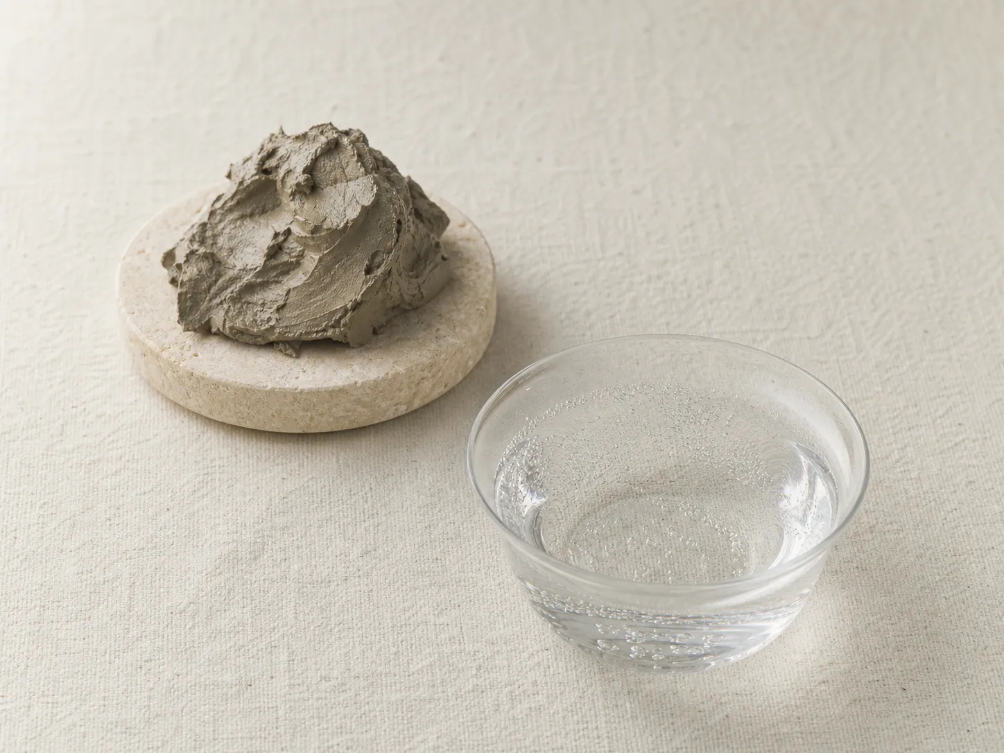 石皿に盛られた泥と、透明な水に細かな泡が立つ静物の印象画像。